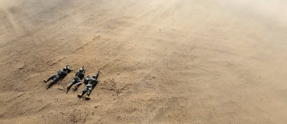Three U.S. soldiers lie prone in the sand